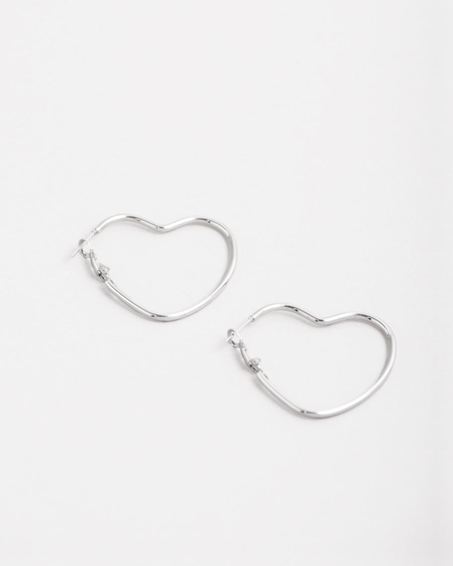 Orecchini Silvia in acciaio inossidabile color argento. Sono un modello a cerchio a forma di cuore ed hanno la chiusura a monachella. Sono rappresentati affiancati e l'orecchino di sinistra è leggermente più in alto di quello a destra.