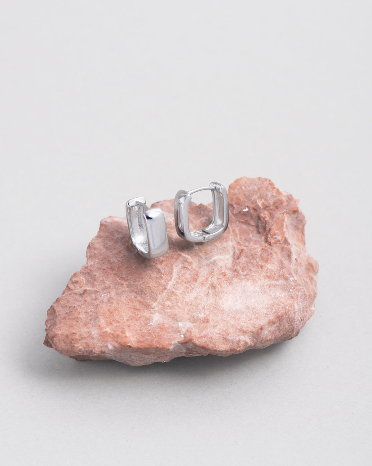 Orecchini Valentina, posati su una roccia dai toni del rosso e del rosa. Hanno una forma quadrata in acciaio lucido color argento.