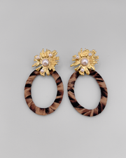 Orecchini Barbara composti da un fiore in acciaio inossidabile color oro e perle dal quale pende un ovale in tessuto maculato. Sono appoggiati su uno sfondo grigio chiaro.