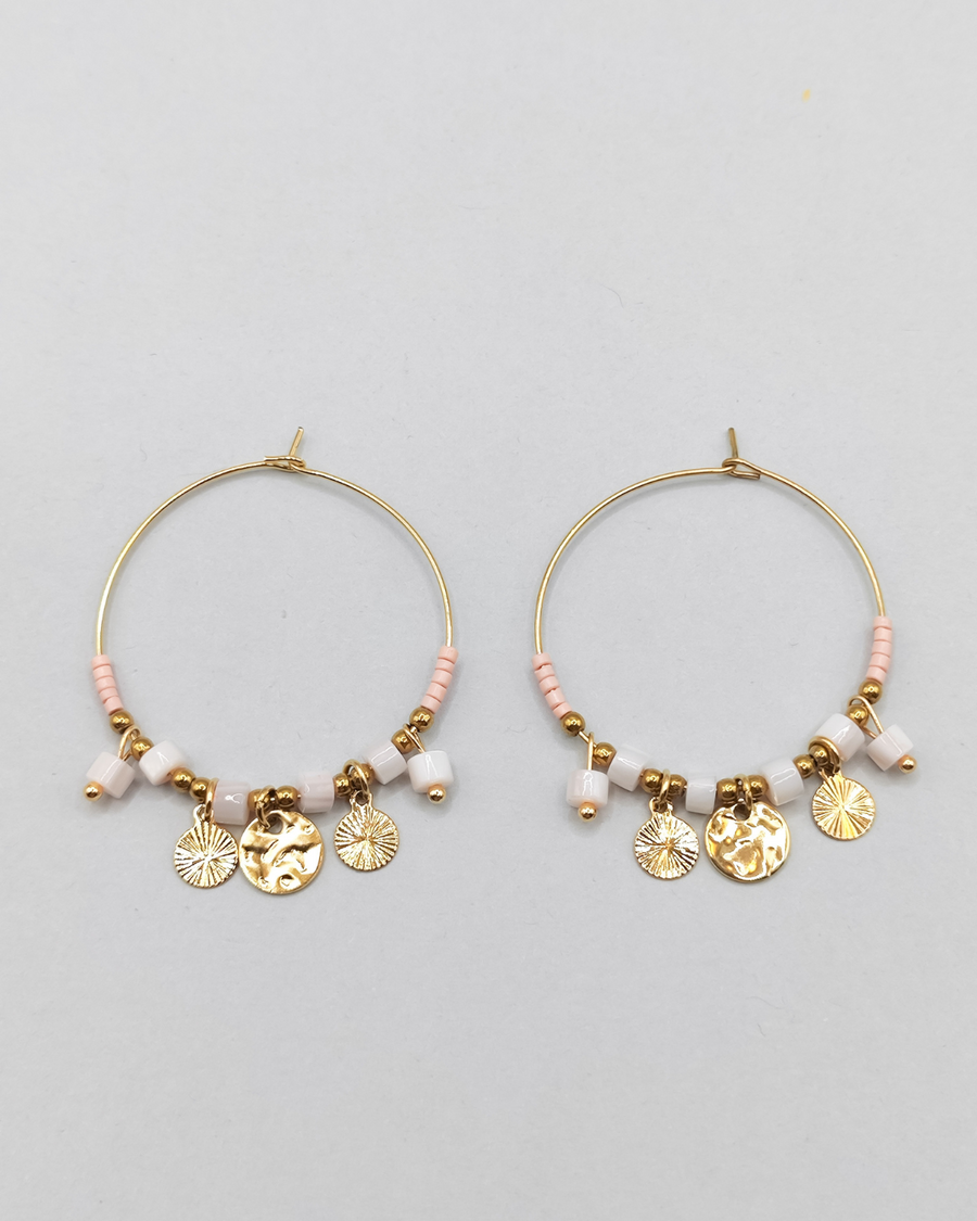 Orecchini Mascia in acciaio inossidabile anallergico color oro. Hanno una forma a cerchio e sono arricchiti da perline e pietre colore rosa e charms dorati.