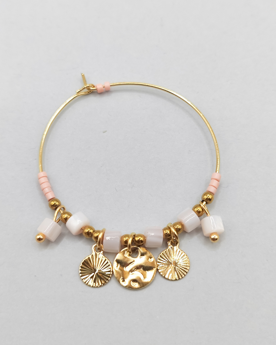 Orecchino Mascia in acciaio inossidabile anallergico color oro. Ha una forma a cerchio ed è arricchito da perline e pietre colore rosa e charms dorati.