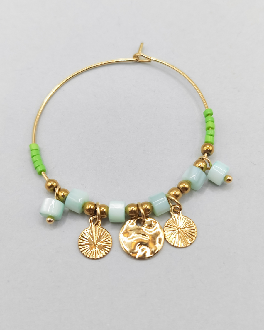 Orecchino Mascia in acciaio inossidabile anallergico color oro. Ha una forma a cerchio ed è arricchito da perline e pietre colore verde e charms dorati.