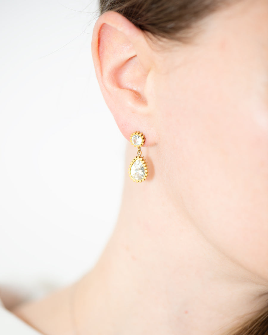 Orecchini Ylenia in acciaio inossidabile color oro indossati. Hanno una forma a bottoncino in strass dal quale pende un ciondolo a forma di goccia, sempre in strass.