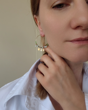 Orecchino a cerchio Mascia in acciaio inossidabile con charms, perle pietre, e cristalli verde. È indossato da una modella bionda con treccia e capelli biondi.