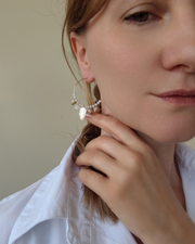 Orecchino a cerchio Viky in acciaio inossidabile con charms, perle pietre, e cristalli bianchi. È indossato da una modella bionda con treccia e capelli biondi.