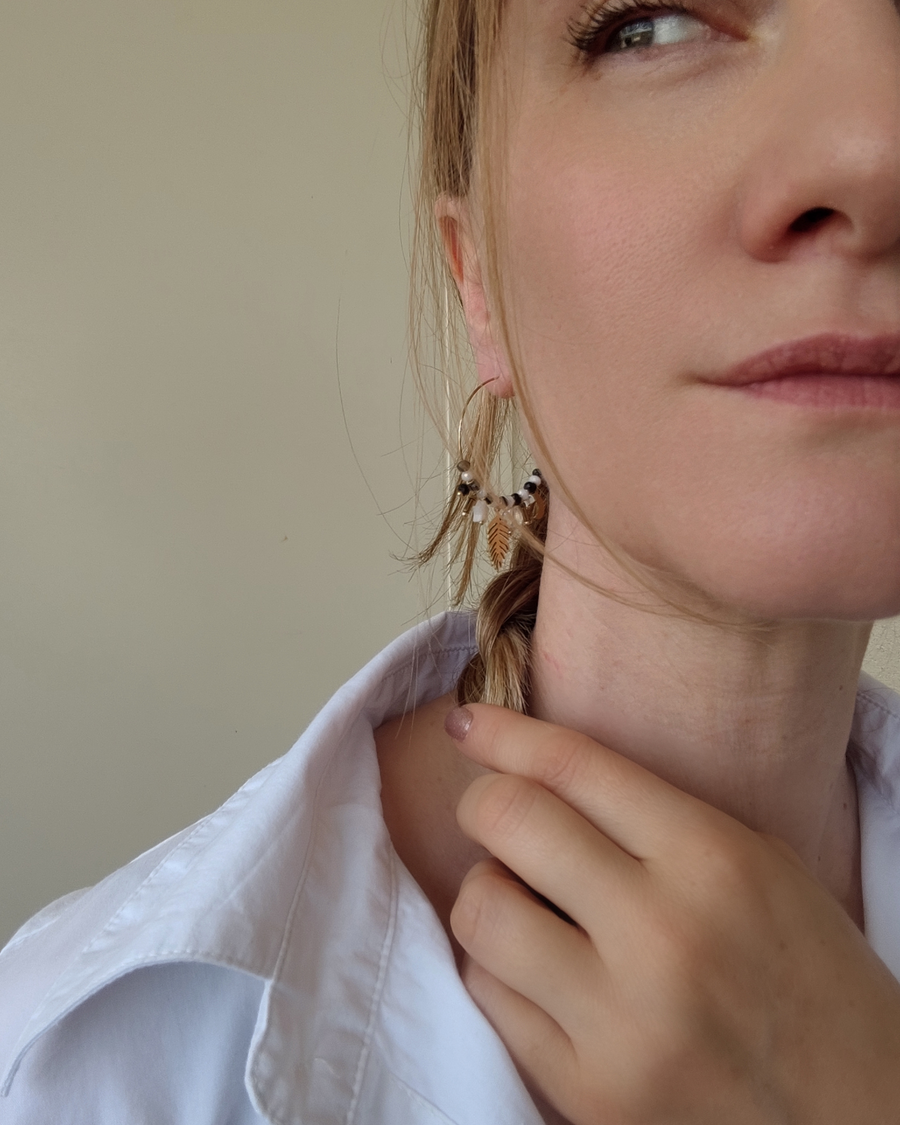 Orecchino a cerchio Viky in acciaio inossidabile con charms, perle pietre, e cristalli neri. È indossato da una modella bionda con treccia e capelli biondi.