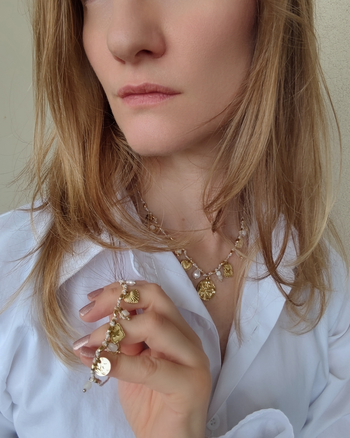 Set Mascia composto da collana e braccale in acciaio inossidabile color oro e filo rosa con charms, perle, pietre e perle indossati da una modella bionda con camicia bianca. La collana è indossata mentre il bracciale è tenuto in mano.