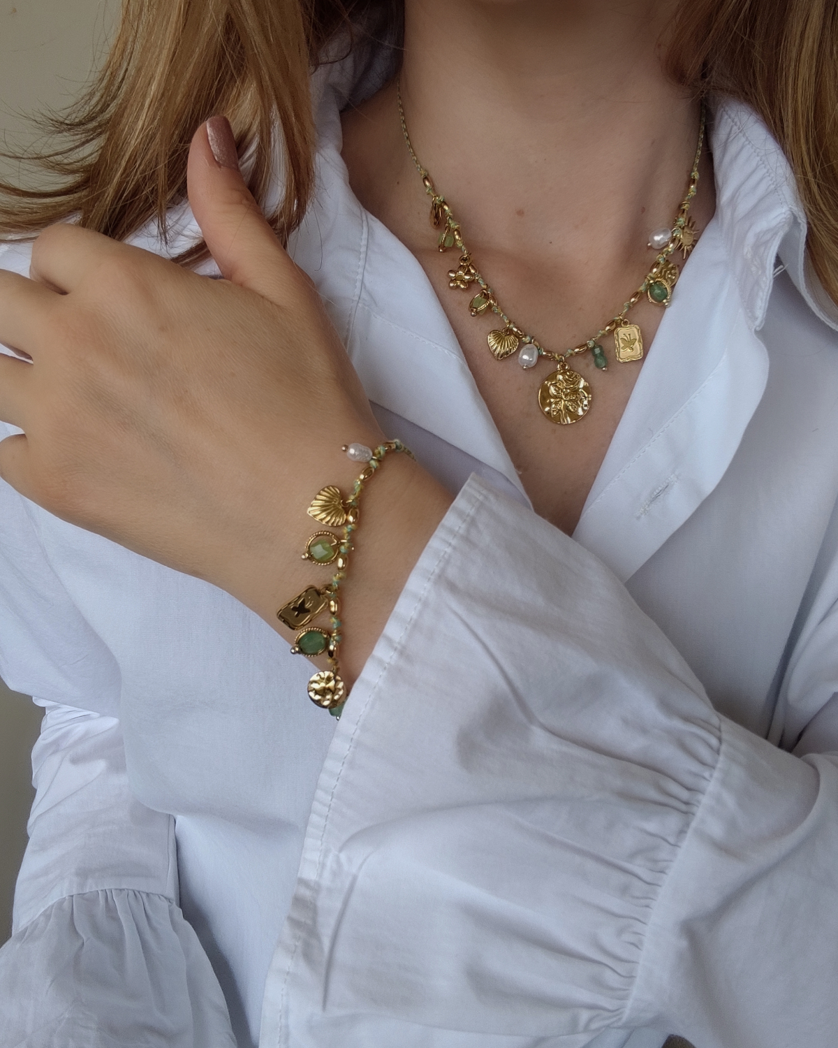 Set Mascia composto da collana e braccale in acciaio inossidabile color oro e filo verde con charms, perle, pietre e perle indossati da una modella bionda con camicia bianca. 